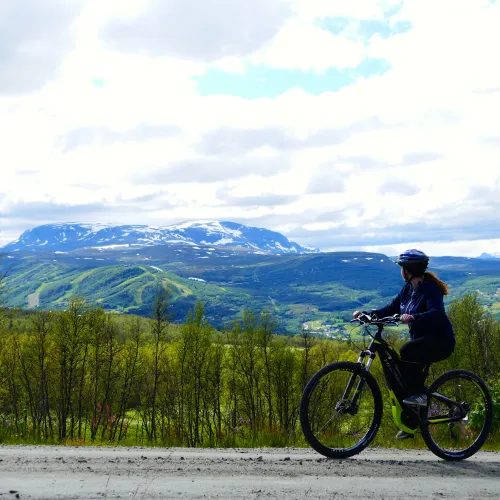 Syklist på grusveg på vei opp Eilevstølen med utsikt over Geilohovda med alpinbakkene og Hallingskarvet i bakgrunn. sommer