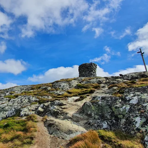 Ustetind fjelltopp på 1376 moh sett nord fra, med stolpe med veiskilt ved siden av. Blå himmel med noen hvite små skyer og store stein med grønn, gulaktig gress.
