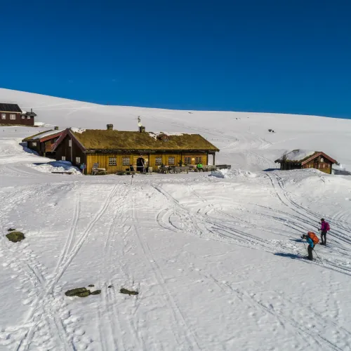 Dronebilde fra Tuva Turisthytte med snø og folk på ski